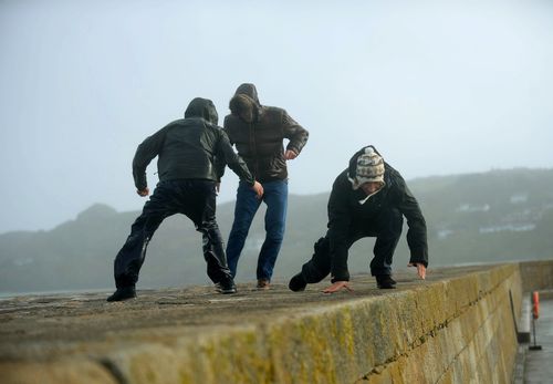 Men struggle to keep their footing amid gusts during storm Ophelia on the wall of East Pier in Howth, Dublin, Ireland. (AAP)