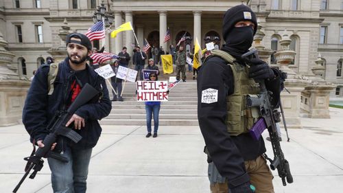 Protesters brandish assault rifles and swastikas at a rally opposing Michigan lockdown laws.