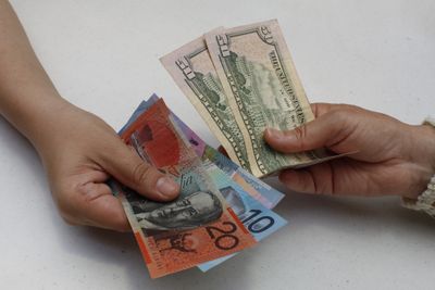 hands exchanging Australian banknotes and American dollars bills