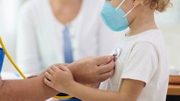 Paediatrician doctor examining sick child in face mask.