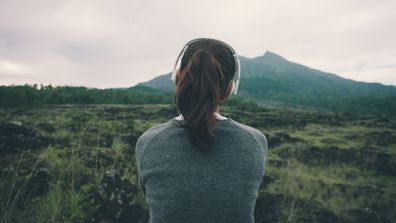 Woman in headphones listening music in nature and at the mountain (intentional pale color style)