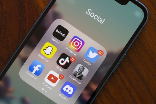 A variety of popular social media apps—BeReal, Instagram, Twitter, Snapchat, TikTok, Clubhouse, Facebook, YouTube, and Discord—are viewed on an iPhone. 