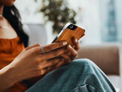 Cropped shot of a woman using a smartphone while relaxing on the sofa at home