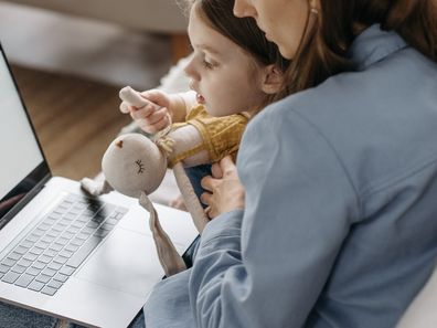 Working mum sits on her laptop with her child. Stock photo.