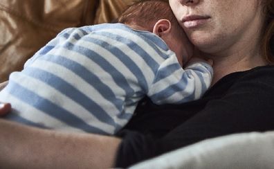 Tired mother holding baby on lounge.