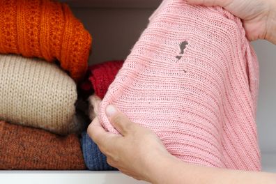 woman hands holding woolen knitted cloth with hole made by moth over wardrobe with stacks cloth on shelf