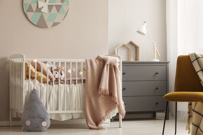 Pillows and toy in white wooden crib with pastel pink blanket in bright nursery