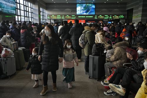 A woman and children wearing face masks walk by masked travelers wait at a departure hall to catch their trains at the West Railway Station in Beijing