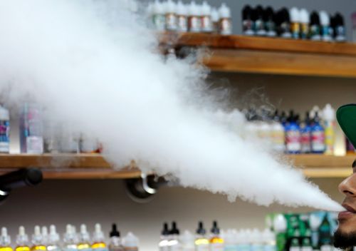 A salesman at a vape shop exhales while using an e-cigarette in Maine, USA.