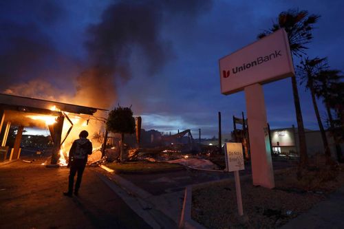 San Diego County sheriff officers stand guard in front of a burning bank building.