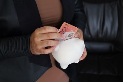 hands of a woman holding an Australian banknote and a piggy bank