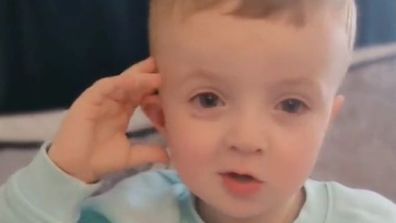 Toddler boy in a blue jumper leaning his head against his hand.
