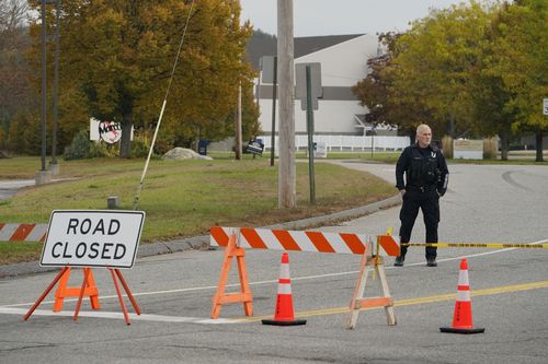 A police officer stands at a road closure near a bowling alley, seen in background, Thursday, Oct. 26, 2023, in Lewiston, Maine. 