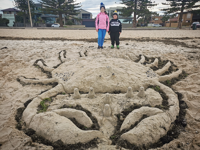 The Devoil family sculpt a giant crab in the sand at a Melbourne beach to cheer up locals in lockdown