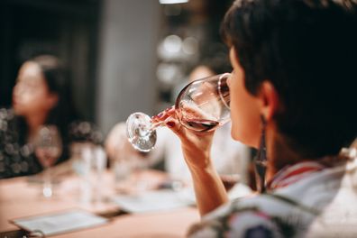 Woman facing away from the camera, drinking a glass of wine