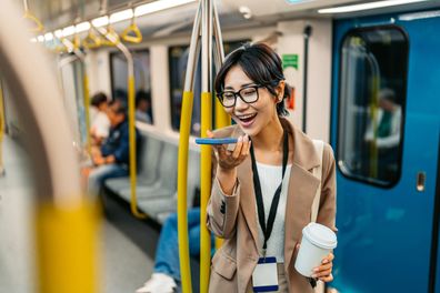 Beautiful young Japanese Asian businesswoman sending a voice message with her phone and drinking coffee while riding a subway in Sydney, Australia.