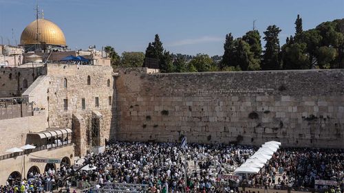 Jewish men pray at the wailing wall, the last remnant of the old Jewish Temple of Jerusalem. In the background is the Dome of the Rock, one of the most sacred shrines in Islam.