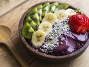 Bowl of acai purée with toppings of banana, kiwi, strawberry and seeds.