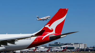 Qantas aircraft on tarmac and Jetstar plane flying in the background