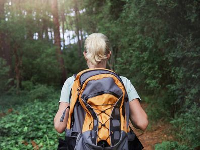 Rear view of a woman wearing a backpack hiking through a forest in nature alone. Female walking on a trail in the outdoors