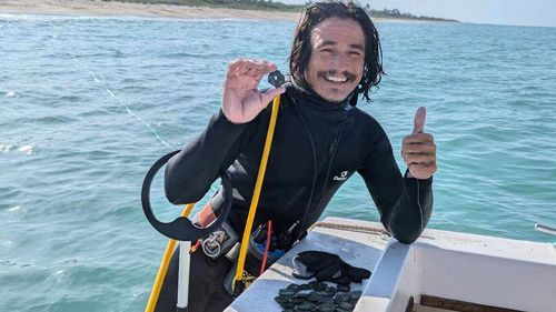 In this undated photo provided by shipwreck salvage company 1715 Fleet- Queens Jewels, LLC, diver Levin Shavers shows coins uncovered from a Spanish shipwreck off the Atlantic coast of Florida.