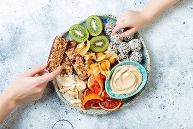 Mother sharing healthy vegan dessert snacks with toddler child.  Concept healthy sweets for children.  Protein Granola Bars, Homemade Raw Energy Balls, Cashew Butter, Toasted Coconut Chips, Fruit Bowl