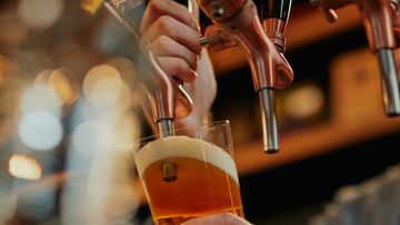 Tattooed caucasian barman pouring beer while standing in pub.