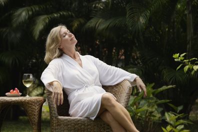 Woman sunbathing and drinking a glass of wine at home. Woman enjoying a glass of wine. Woman in a robe.