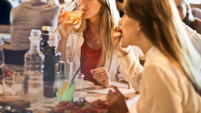 Stock image of two women eating and drinking wine.