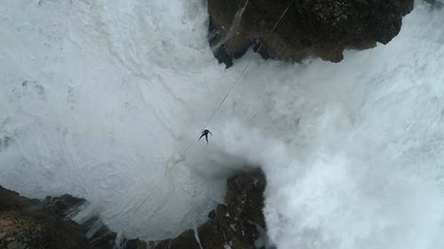 The daredevil can be seen being knocked off the cable by a surge of water from the raging ocean beneath him, leaving him dangling mid-air (Supplied).