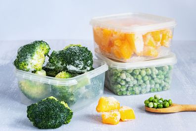 Frozen vegetables. Frozen broccoli, peas and pumpkin in plastic boxes and a wooden spoon on grey table