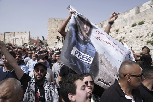 Mourners hold a banner depicting slain Al Jazeera veteran journalist Shireen Abu Akleh as they walk from the Old City of Jerusalem to her burial site, Friday, May 13, 2022. Abu Akleh, a Palestinian-American reporter who covered the Mideast conflict for more than 25 years, was shot dead Wednesday during an Israeli military raid in the West Bank town of Jenin.(AP Photo/Ariel Schalit)