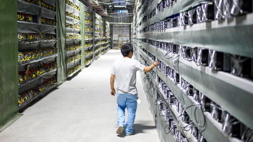 A technician walks by rows of super computers inside a Bitcoin mining facility in West Sichuan. The facility's 10,000 super computers solve mathematical equations around the clock to produce the virtual currency.