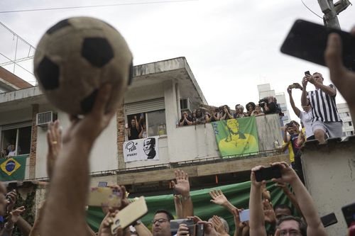 People watch the funeral procession of Brazilian soccer great Pele pass by the home of Pele's mother, where members of his family stand on the balcony, as his remains are taken from Vila Belmiro stadium to the cemetery in Santos, Brazil, Tuesday, Jan. 3, 2023.  