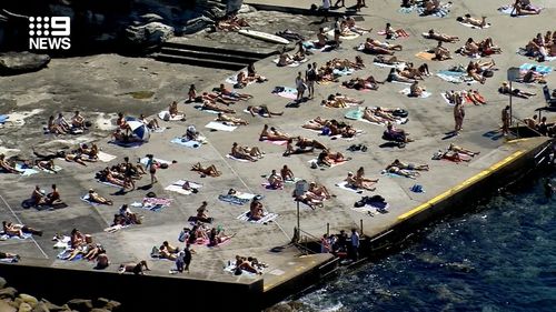 At Clovelly people appear to be spaced out on the concrete at the water's edge.