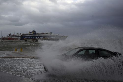 A car drives through seawater from crashing waves on the road during bad weather at the port of Rafina, east of Athens.