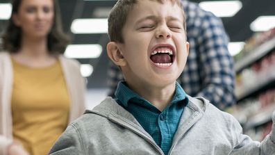 Naughty boy running around supermarket with disappointed parents in background.