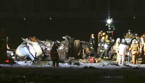 Firefighters are seen near the part of the burnt Japanese Coast Guard aircraft on the runway of Haneda airport on Tuesday, Jan. 2, 2024 in Tokyo, Japan. A passenger plane collided with the Japanese coast guard aircraft and burst into flames at the airport on Tuesday, officials said. (Kyodo News via AP)