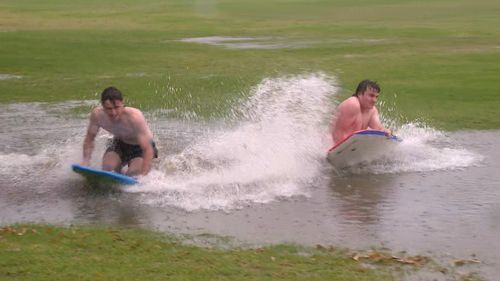 Two men play on boogie boards on a flooded Chiswick oval.