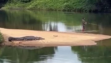 A man has been filmed fishing as a croc lays metres behind him on a riverbank near Cairns.