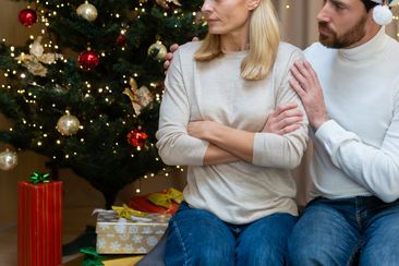 A husband calms his wife and tries to make peace, a quarreling couple sits on the sofa at home near the Christmas tree, a shot of the family celebrating the New Year.