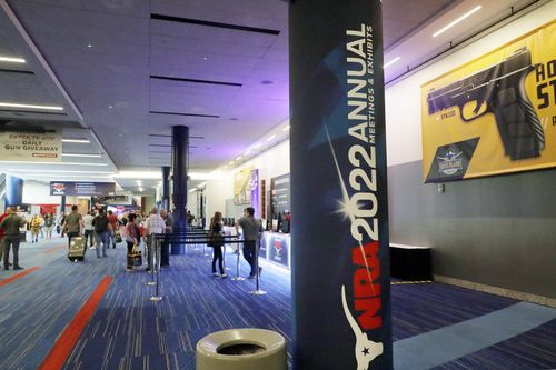 People gather by booths near some of the signage in the hallways outside of the exhibit halls at the NRA Annual Meeting held at the George R. Brown Convention Center Thursday, May 26, 2022, in Houston. (AP Photo/Michael Wyke)