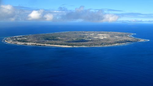 ILHA NAURU: O país inteiro visto de cima - ilha cercado pelo recife de coral - a ilha oval tem um cinturão costeiro estreito onde estão localizados assentamentos, o interior conhecido como 'topside' é um platô estéril de pináculos de calcário irregulares devido aos danos ambientais causados ​​pela mineração de fosfato - yaren e o aeroporto à esquerda - o oceano -sul.
