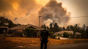 A policeman watches bushfires as they approach homes located on the outskirts of the town of Bargo on December 21, 2019 in Sydney, Australia