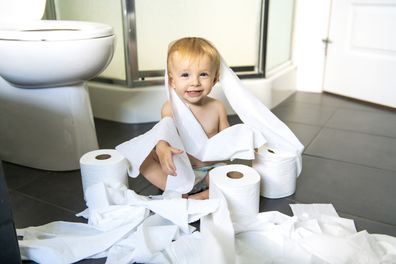 A Toddler ripping up toilet paper in bathroom
