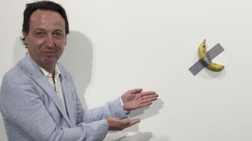 Gallery owner Emmanuel Perrotin poses next to Italian artist Maurizio Cattlelan's "Comedian" at the Art Basel exhibition in Miami Beach, Florida.