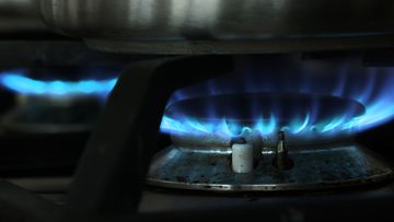 A gas flame burns under a pot on a gas stove top.