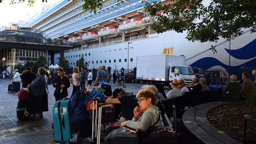 Passengers sit with their luggage after disembarking from the Ruby Princess cruise ship at the Overseas Passenger Terminal in Circular Quay, Sydney