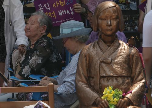 Two former South Korean victims sit next the statue symbolising a comfort woman in Seoul on August 15, National Liberation Day.