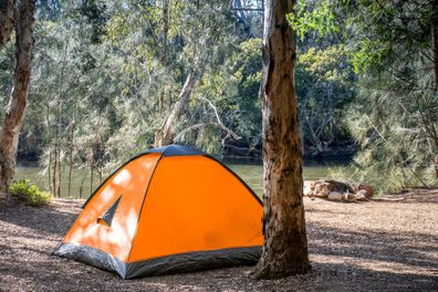 Orange tent at the campsite surrounding by nature on the river bank. Camping and recreation